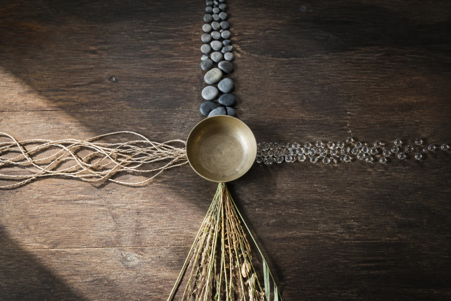 Four paths of stones, cord, glass beads and reeds converging into a brass bowl.